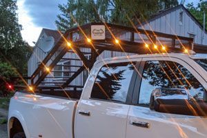 A white truck with a roof rack and lights on it is parked in front of a house.