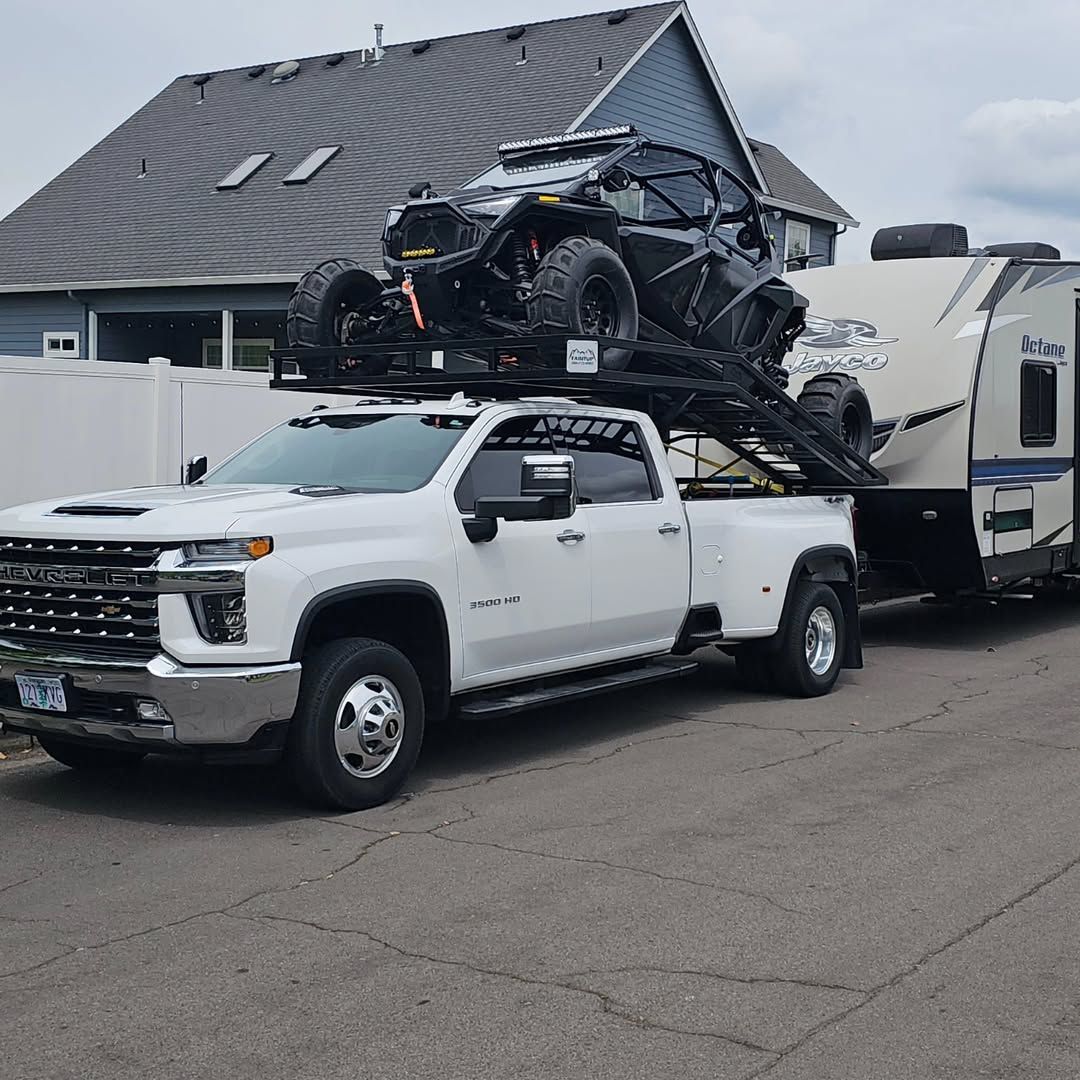 A white truck is towing a trailer with two atvs on top of it.