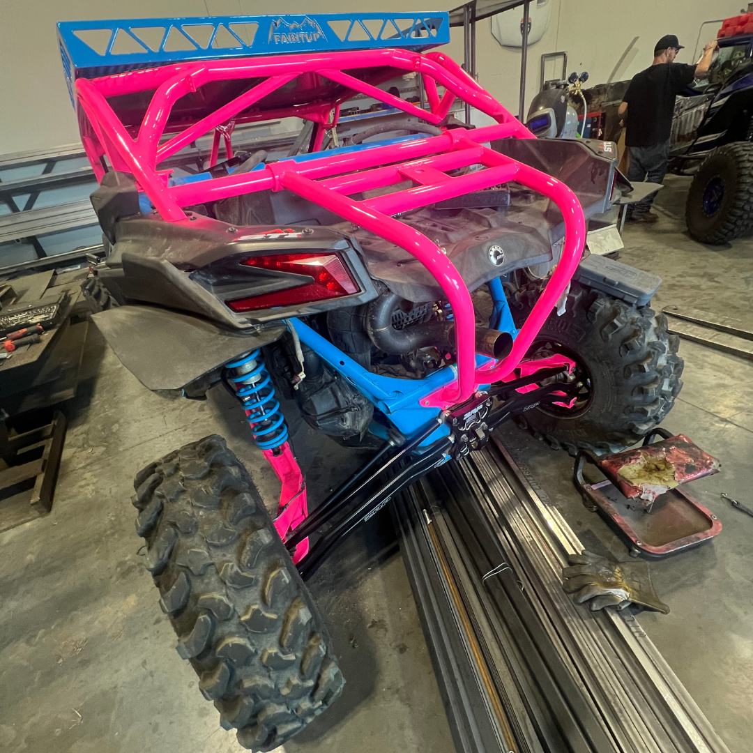 A pink and blue atv is sitting on a track in a garage.