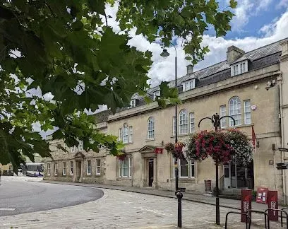 Stone building with arched windows, flower baskets, and a bus in the background. Green leaves in the foreground.