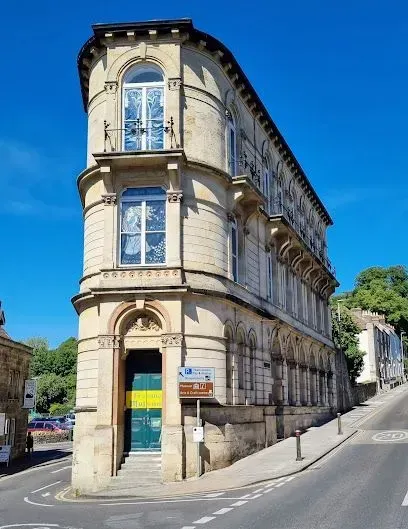 Three-story building with curved facade and arched windows on a street corner under a blue sky.