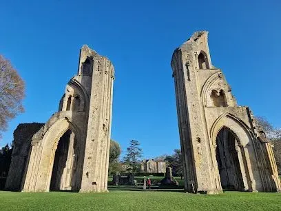 Ruined stone arches of Glastonbury Abbey against a clear blue sky.