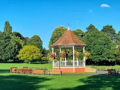 Bandstand in park with green grass, trees, and blue sky.