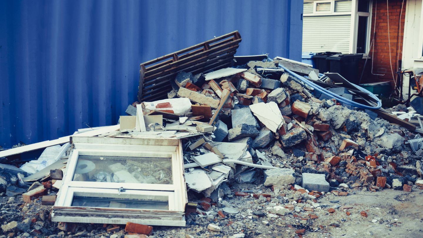 Pile of construction debris with a discarded window frame against a blue wall.