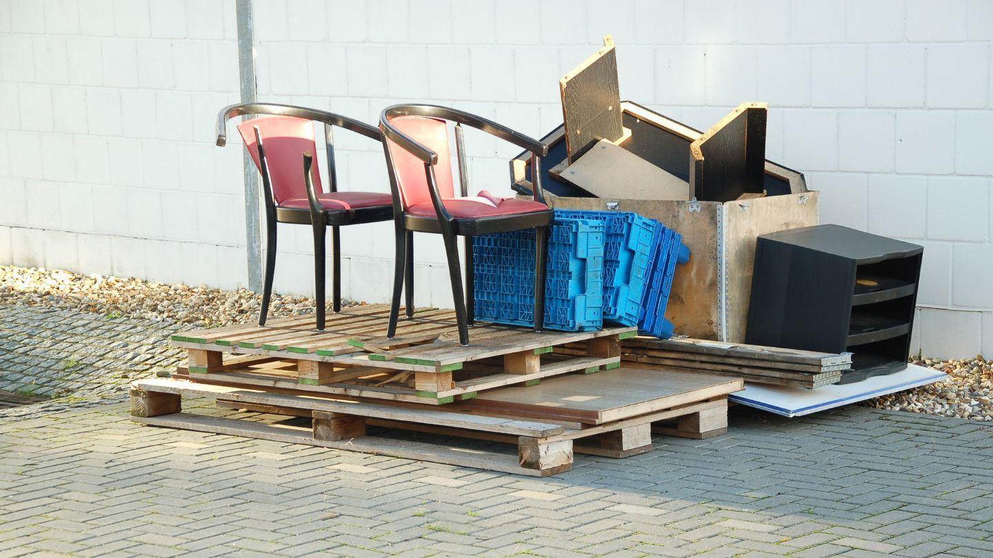 Pile of discarded furniture and debris on wooden pallets, against a white wall.