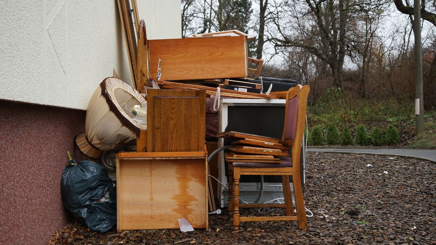 Pile of discarded wooden furniture and trash bags leaning against a building exterior.