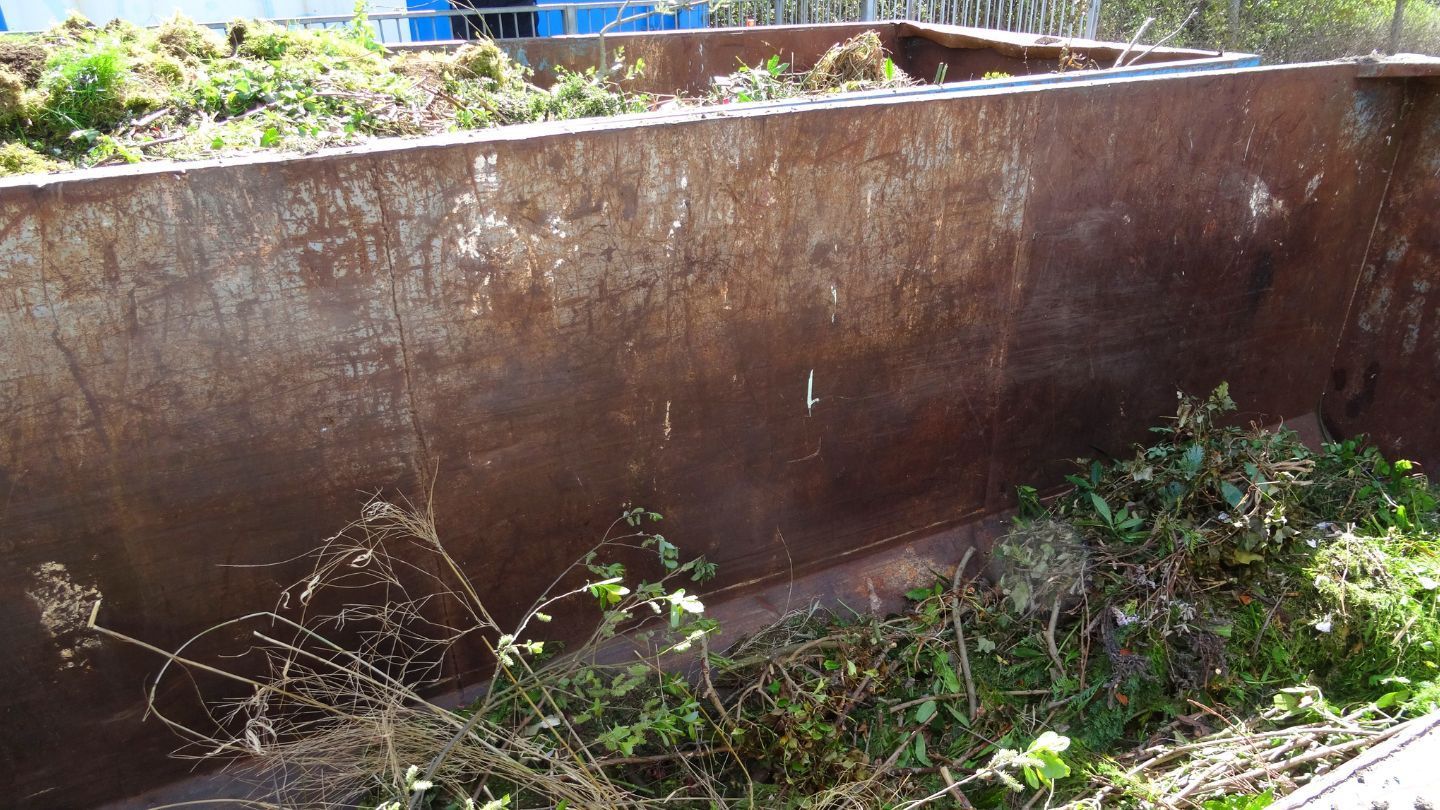 Rusty metal dumpster filled with green yard waste.