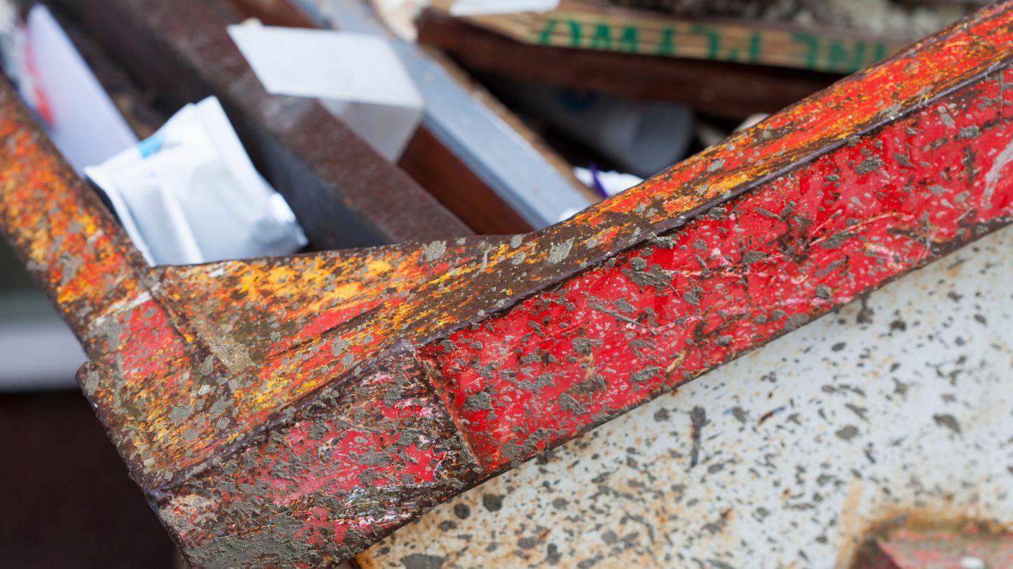 Close-up of a rusted, orange and red metal container corner filled with trash.