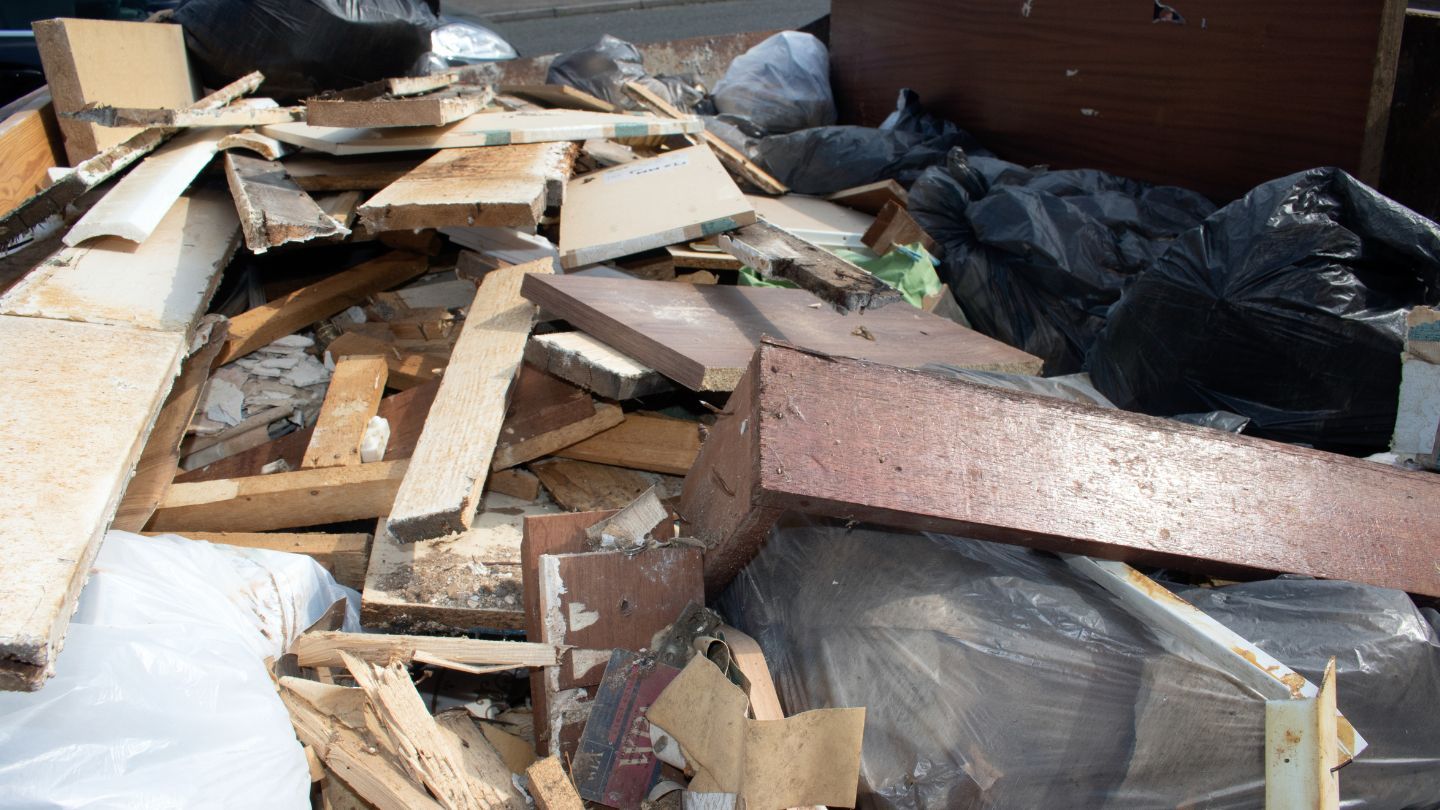 Pile of construction debris and trash in a dumpster. Includes wood, drywall, and garbage bags.
