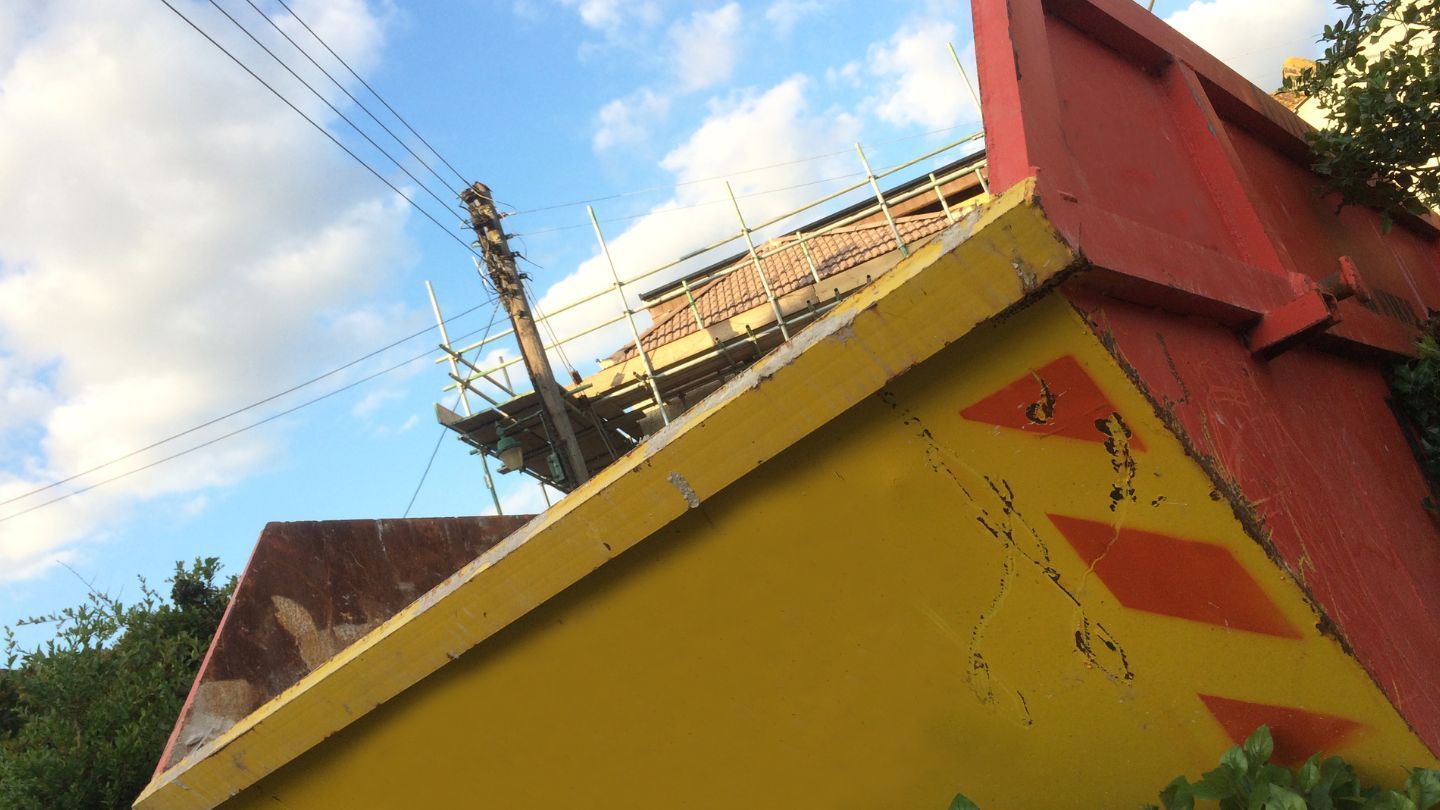 Yellow and red building with scaffolding on roof, against cloudy sky.