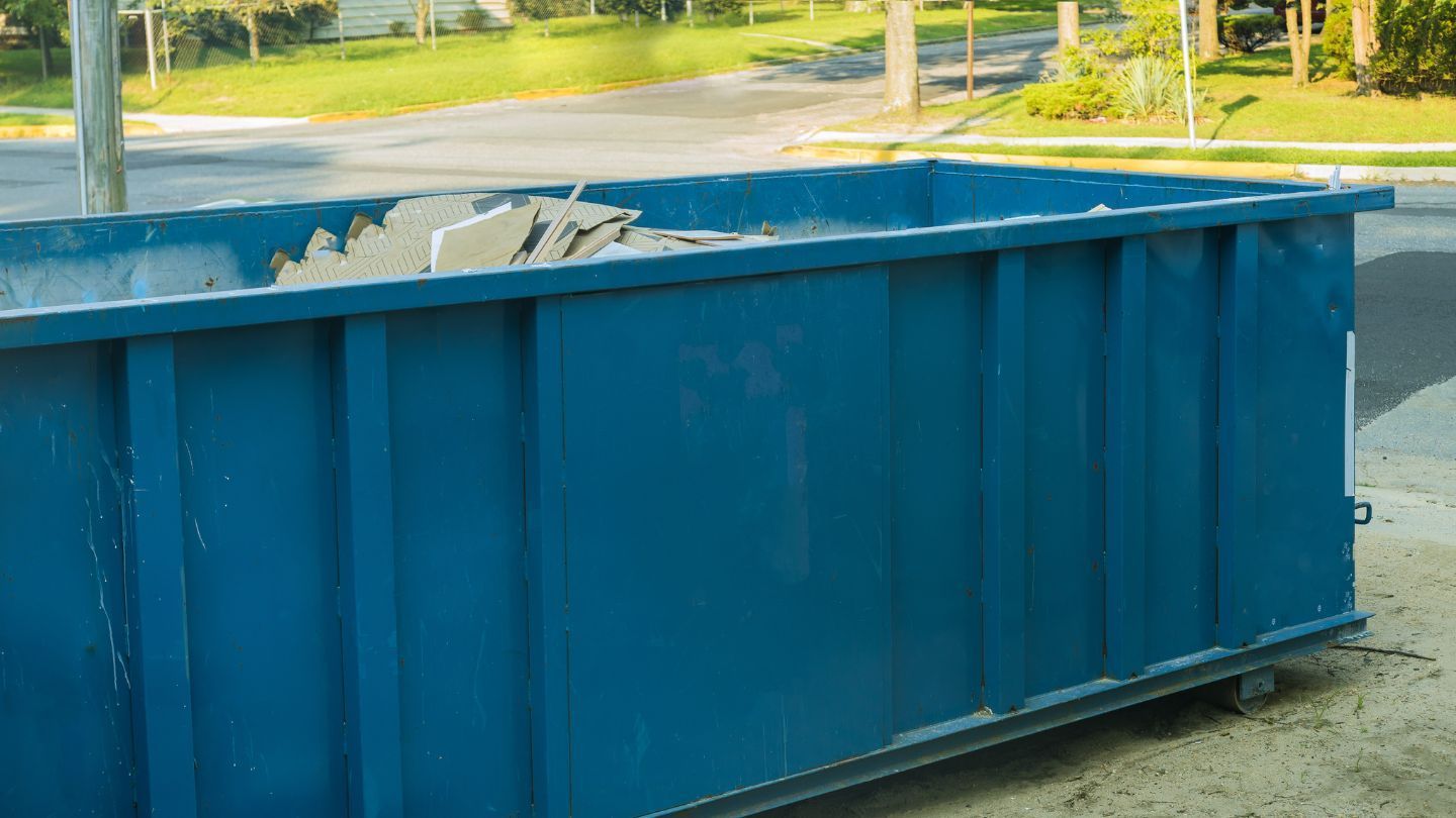 Blue dumpster filled with construction debris, parked outside on a sunny street.