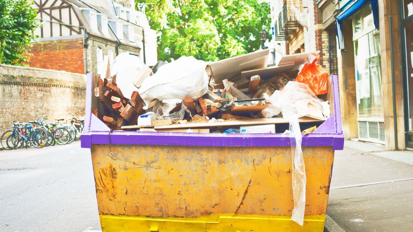 Yellow and purple overflowing dumpster on a street with bikes and brick buildings.