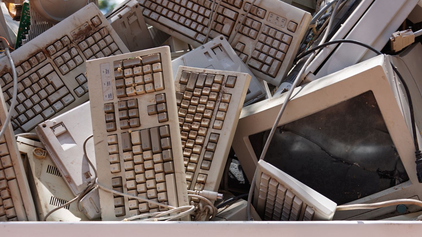 Pile of old, yellowed computer keyboards and monitors, likely in a recycling bin.