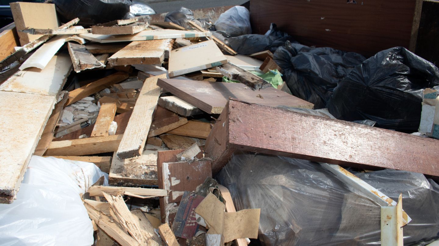 Pile of wood and debris, including boards and black garbage bags, in a container.