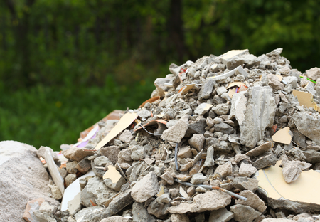 Pile of construction debris in front of blurred green foliage.