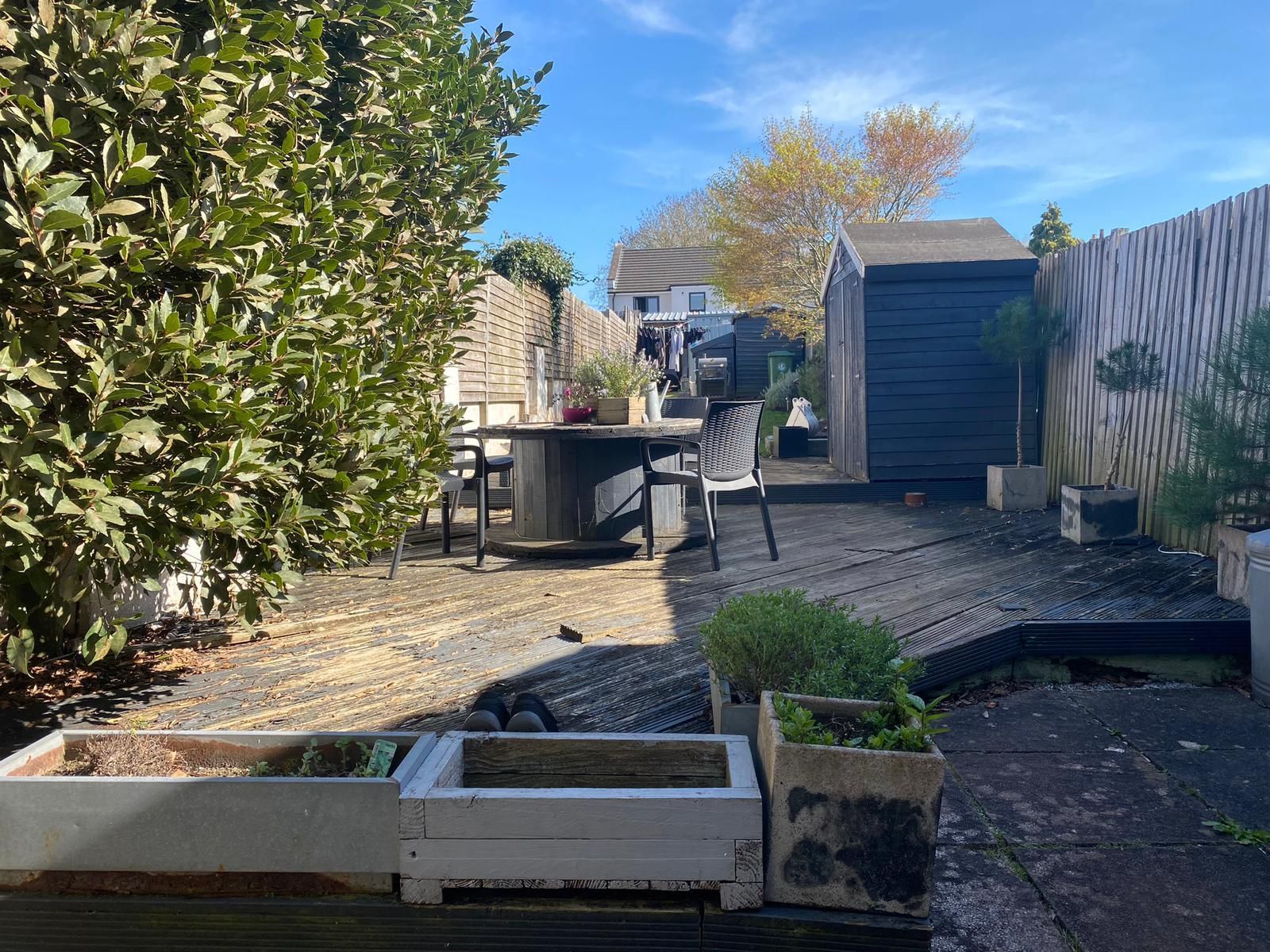 Backyard garden with raised beds, gravel paths, a shed, and a patio table in bright sunlight