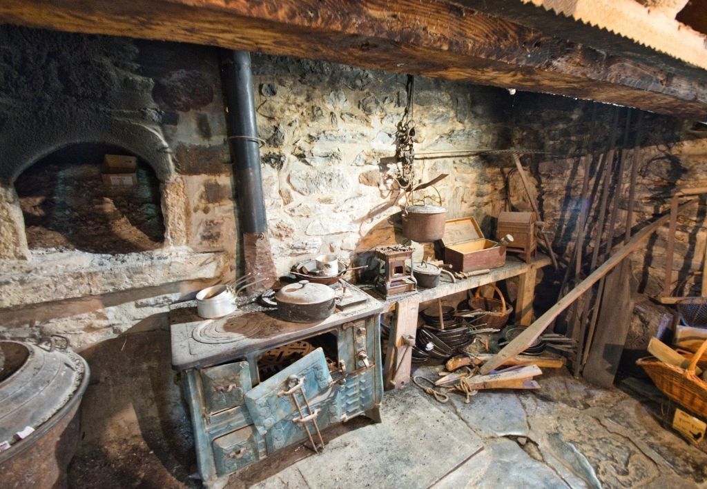 Rustic kitchen interior with stone walls, stove, and cooking utensils.