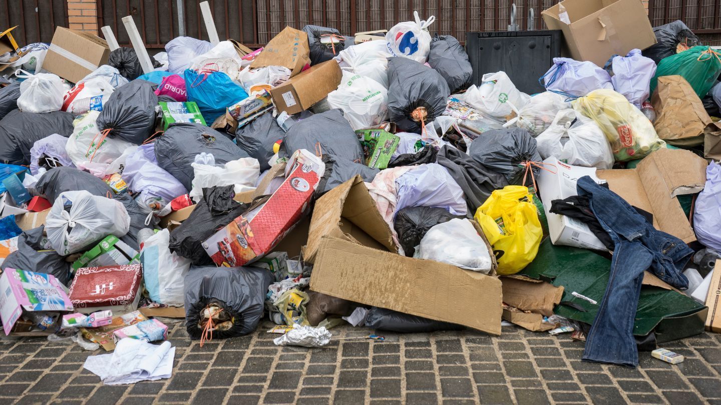 Pile of trash bags, cardboard boxes, and debris overflowing onto a brick surface.