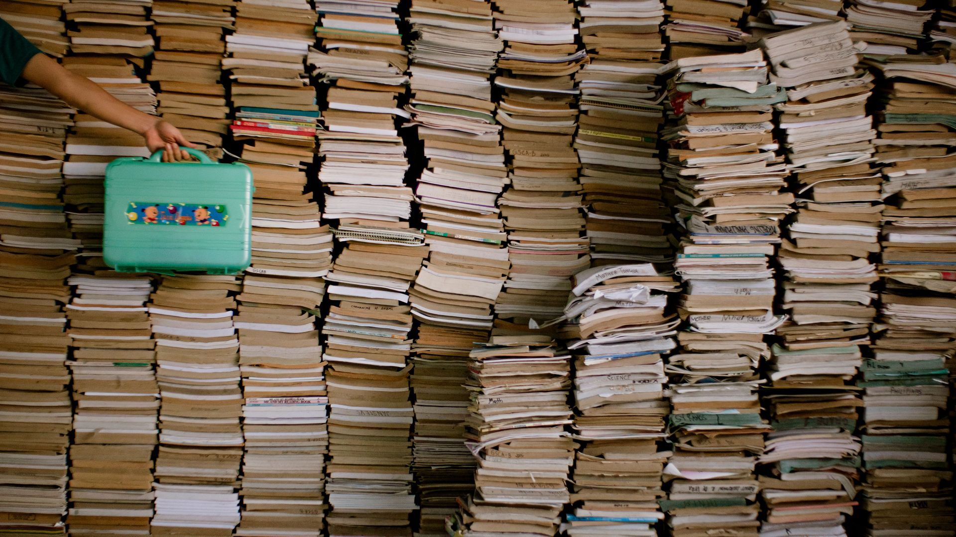 Stacks of worn paper files piled high, with a turquoise notebook on the left.