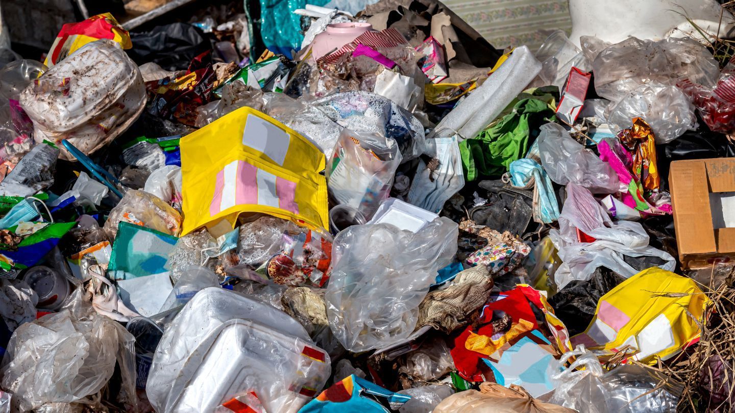 Pile of trash: plastic bags, boxes, food wrappers, and other waste in various colors, scattered.