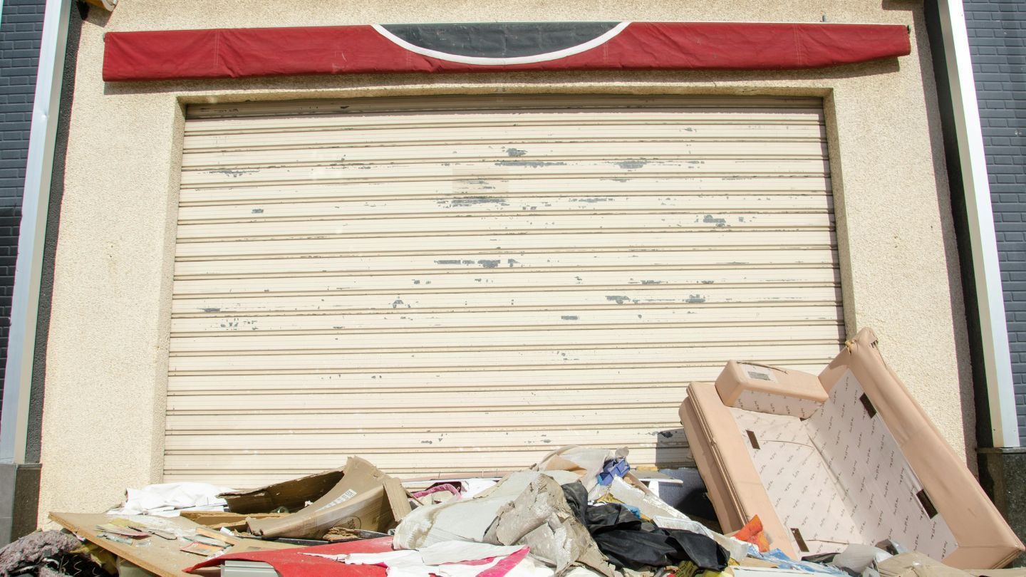 A closed, weathered storefront with a red awning. Debris and furniture clutter the entrance.