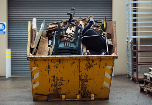 Yellow dumpster overflowing with debris; outside a building.