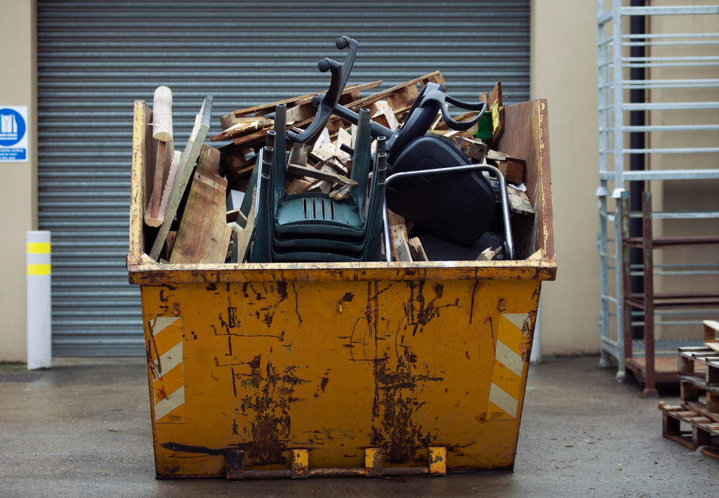 Yellow dumpster filled with metal scraps and debris in front of a closed garage door