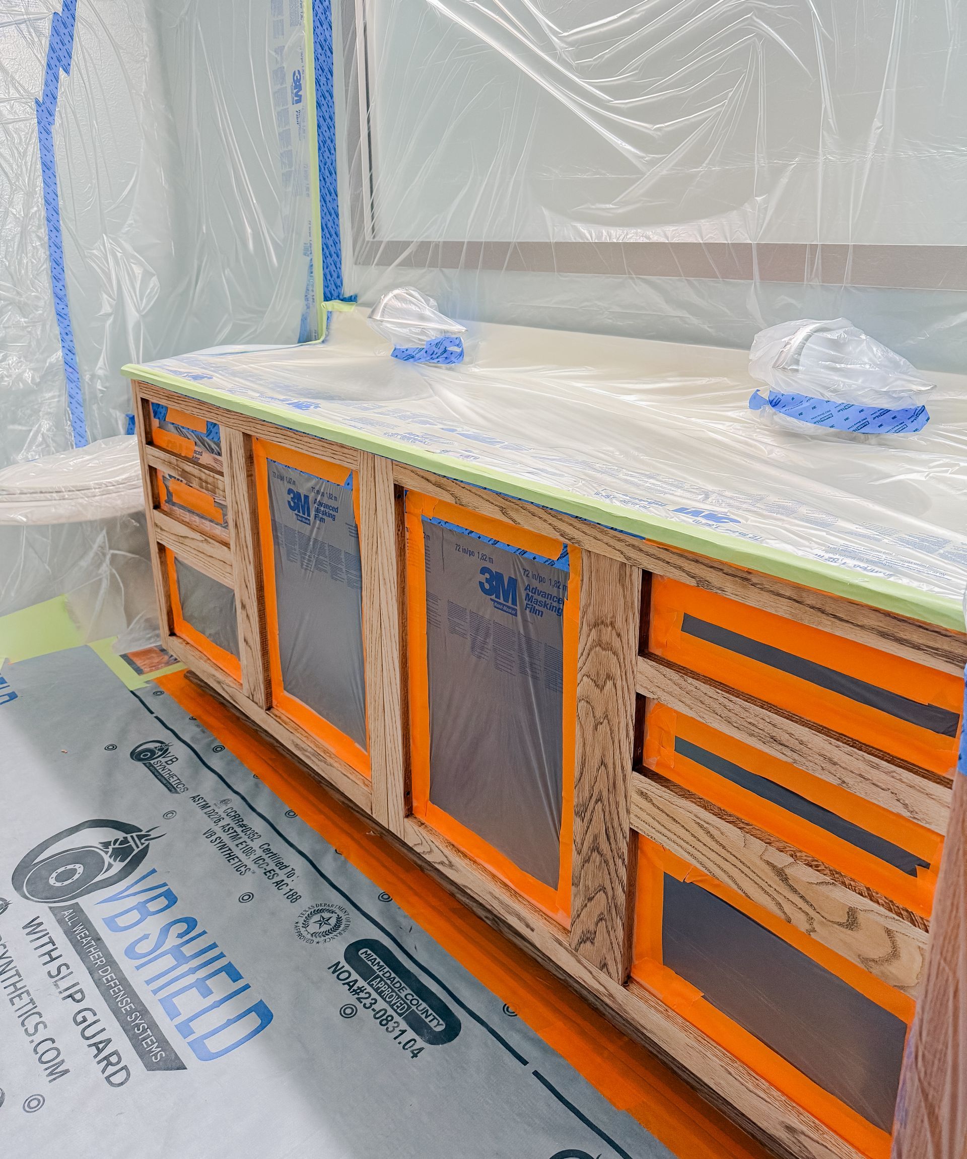 Vanity cabinet under construction, covered in plastic sheeting and tape.