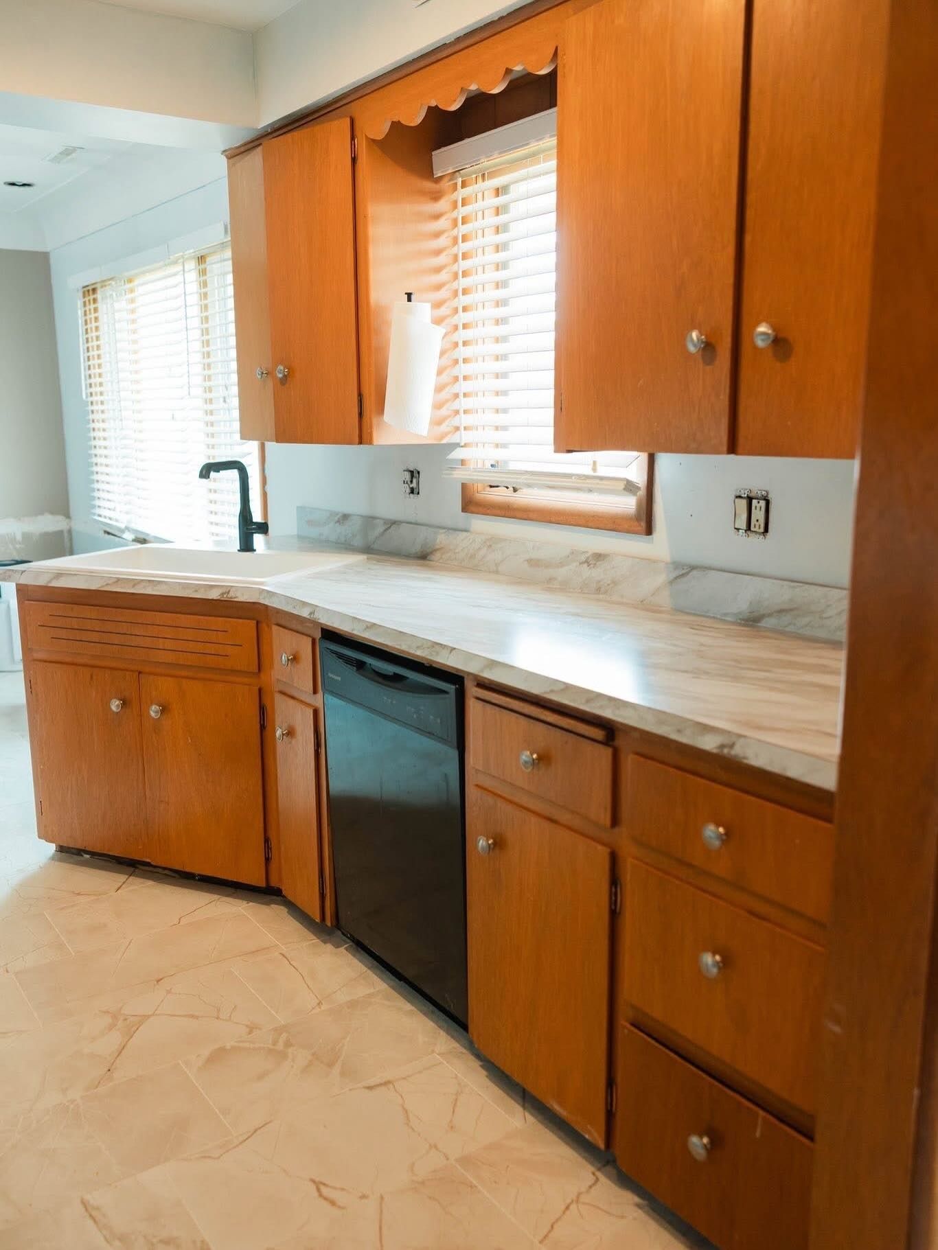 Kitchen with light wood cabinets, a black dishwasher, and a marble countertop.