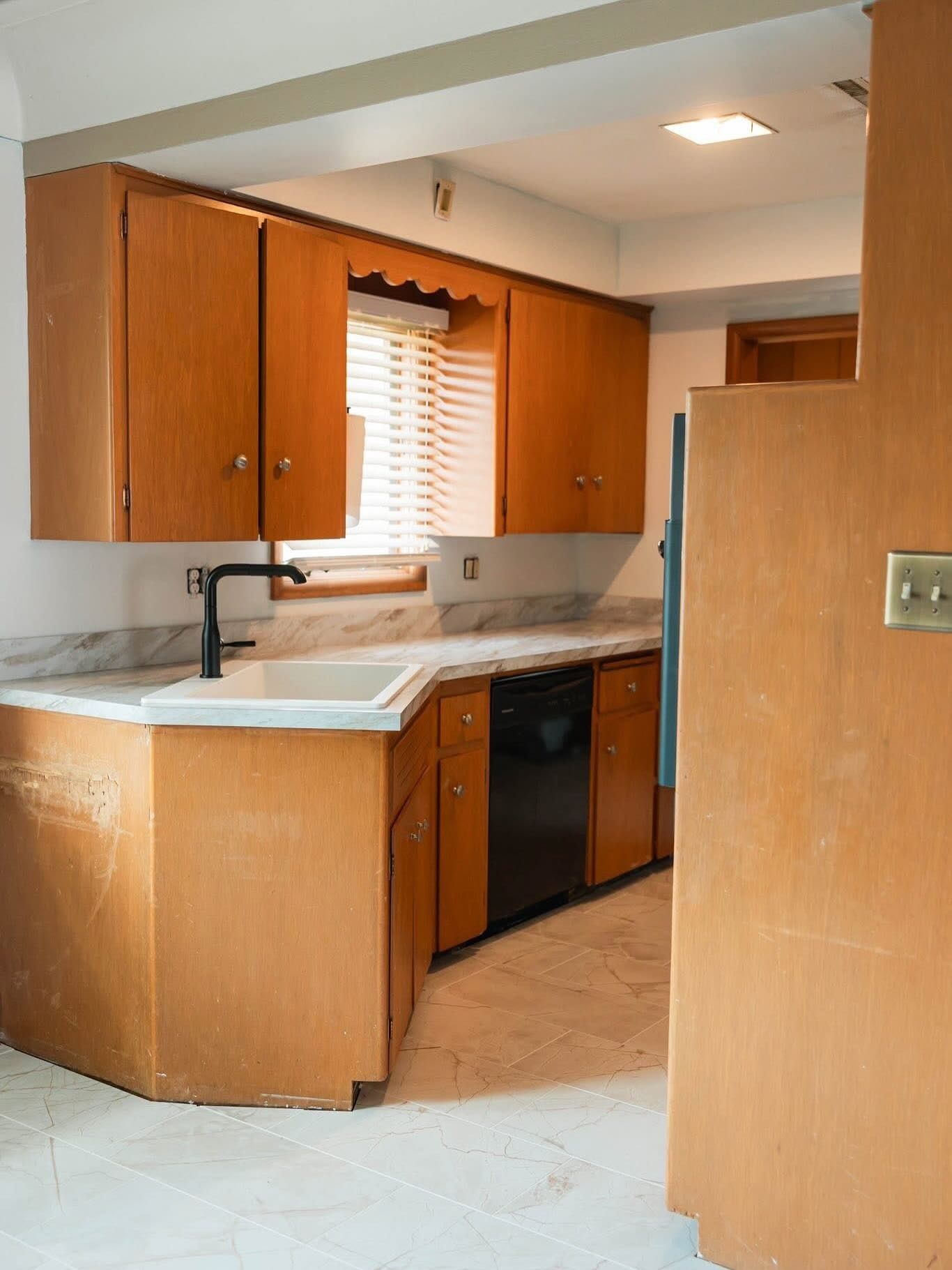 Kitchen with light-colored cabinets, black dishwasher, and a white sink and countertop.