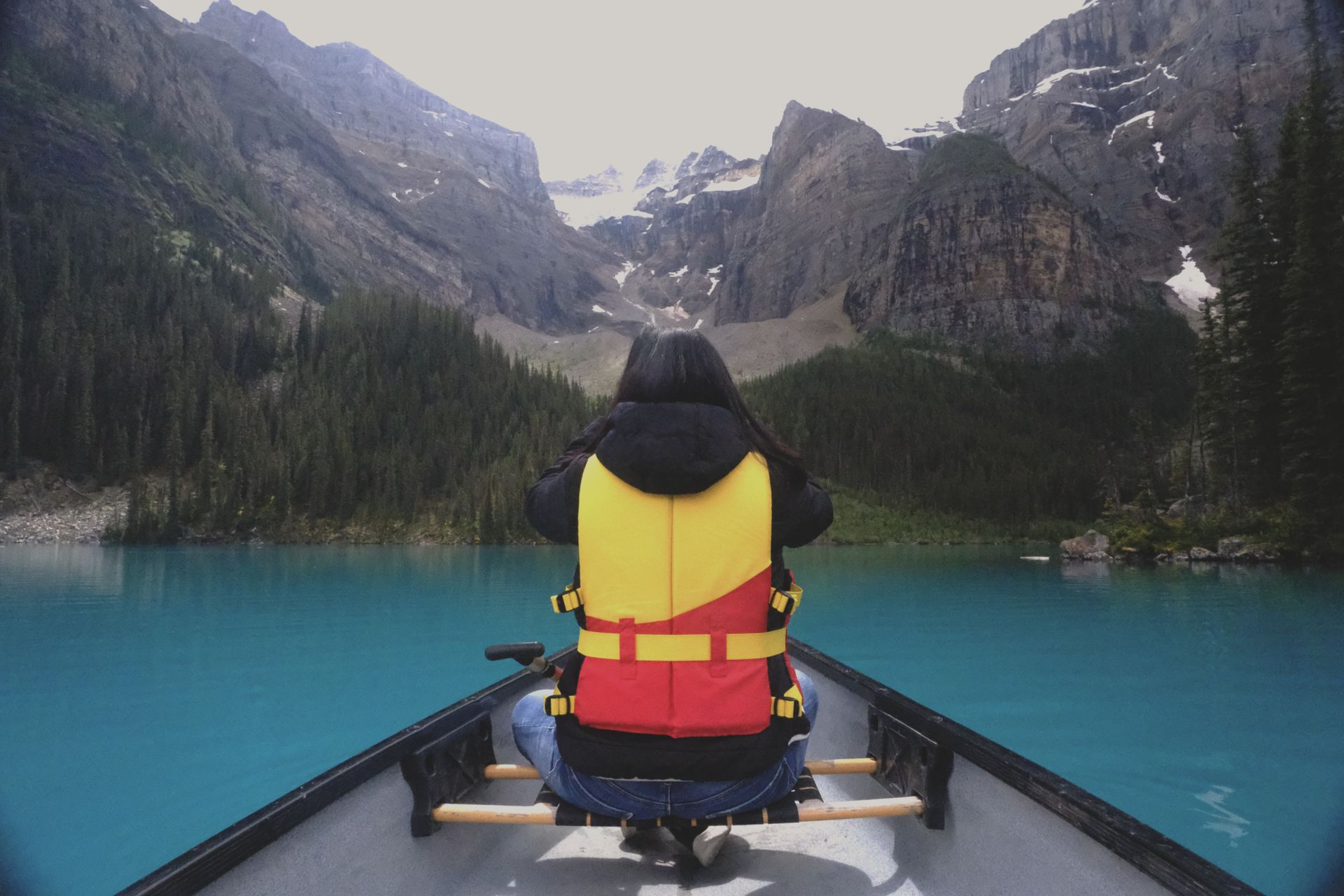 Guest canoeing on turquoise Moraine Lake with mountain peaks reflection, Banff Bear Travel optional canoe experience