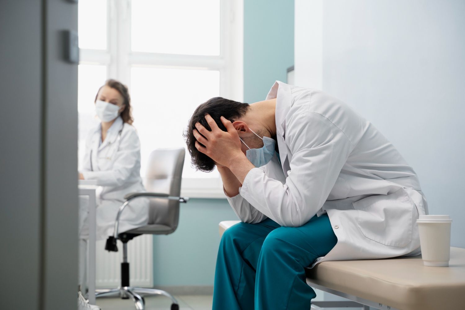 A doctor is sitting on a bench with his head in his hands.