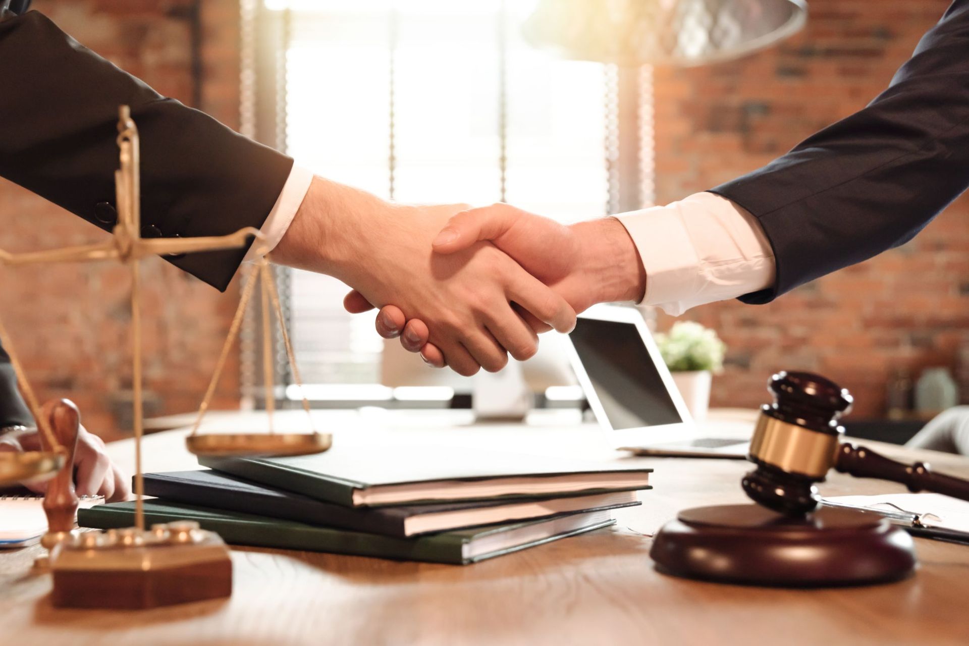 Two men are shaking hands in front of a judge 's gavel and scales of justice.