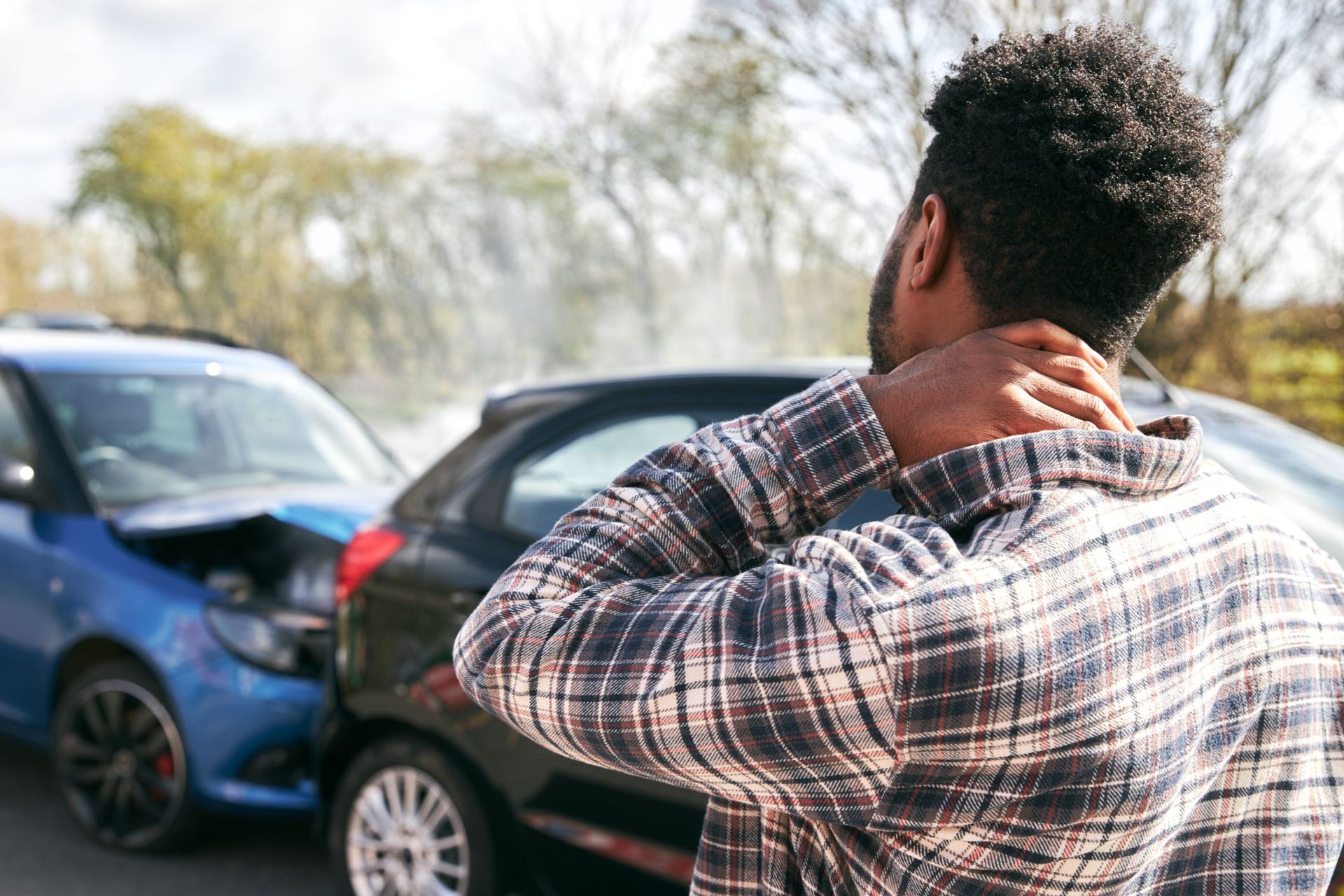 A man is holding his neck in pain in front of a car accident.