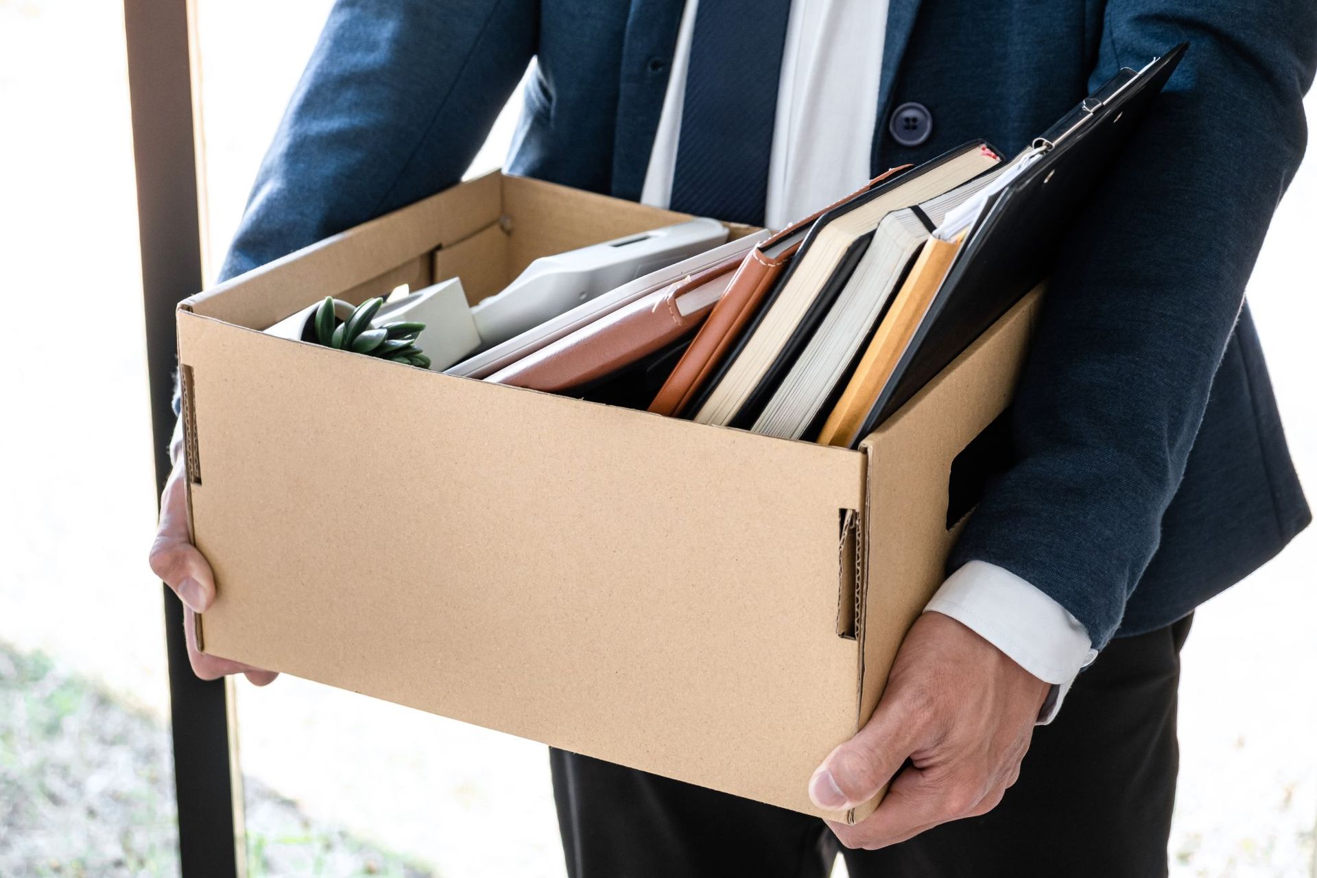 A man in a suit is holding a cardboard box filled with his belongings.
