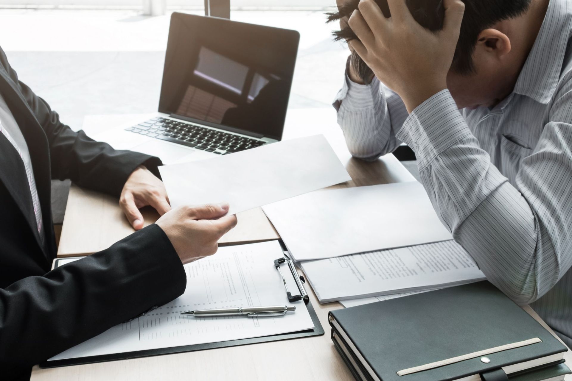 A man is sitting at a desk with his head in his hands while a woman talks to him.
