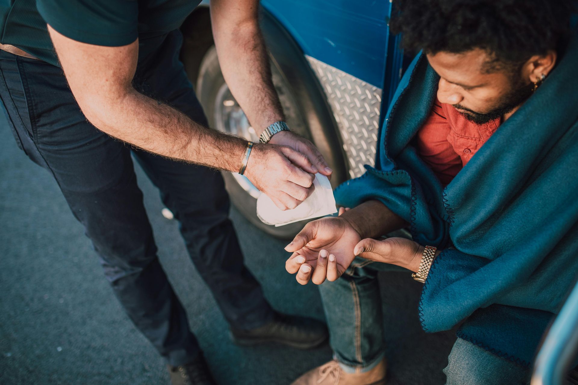 A man is wrapping another man 's arm in a blue blanket.