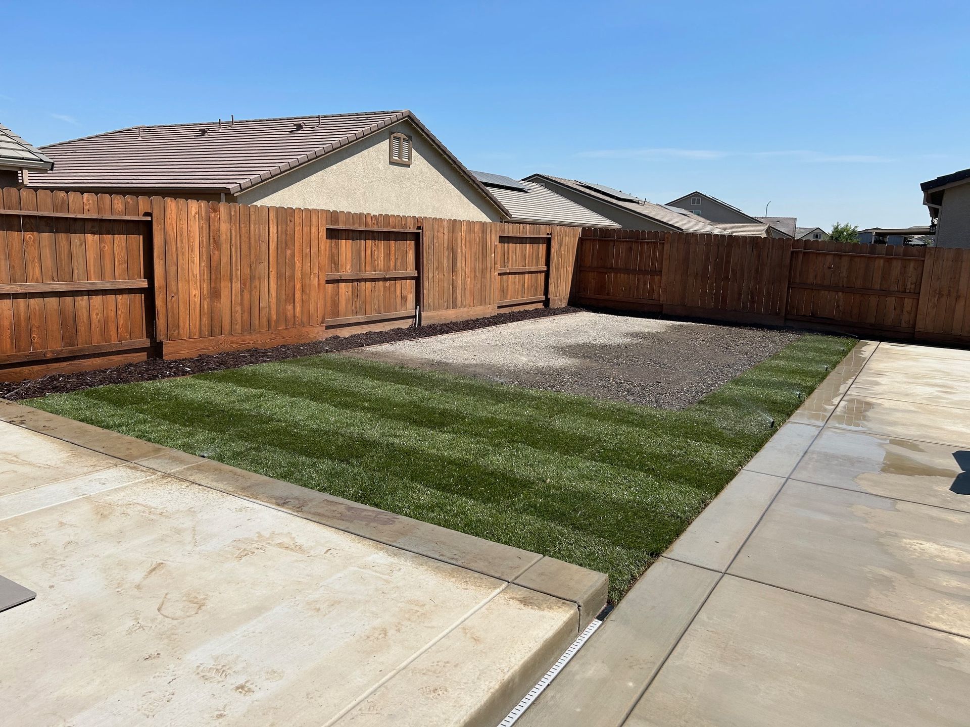 A backyard with a wooden fence and a lush green lawn.