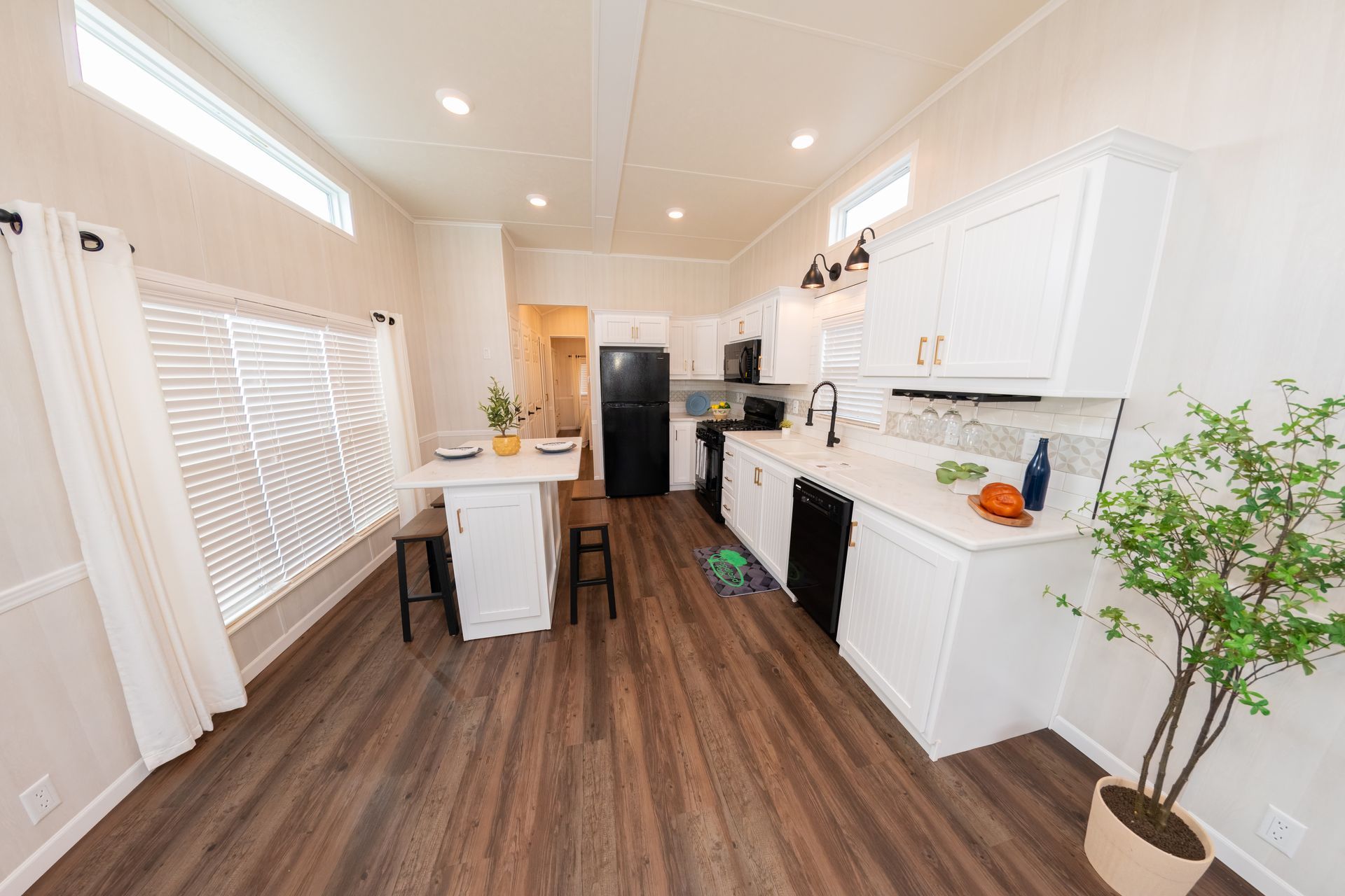 a kitchen in a mobile home with wooden floors and white cabinets .