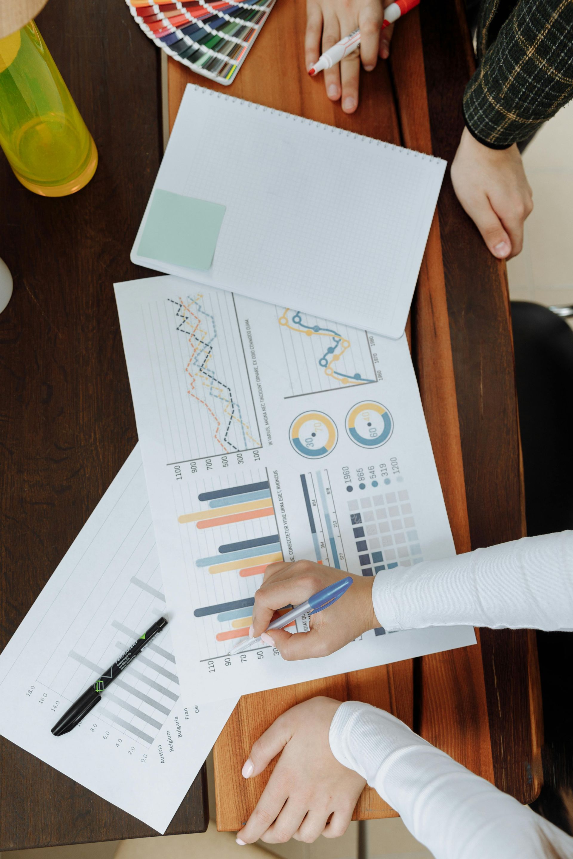 People collaborating over charts and graphs on a wooden table with a color palette and pens nearby.