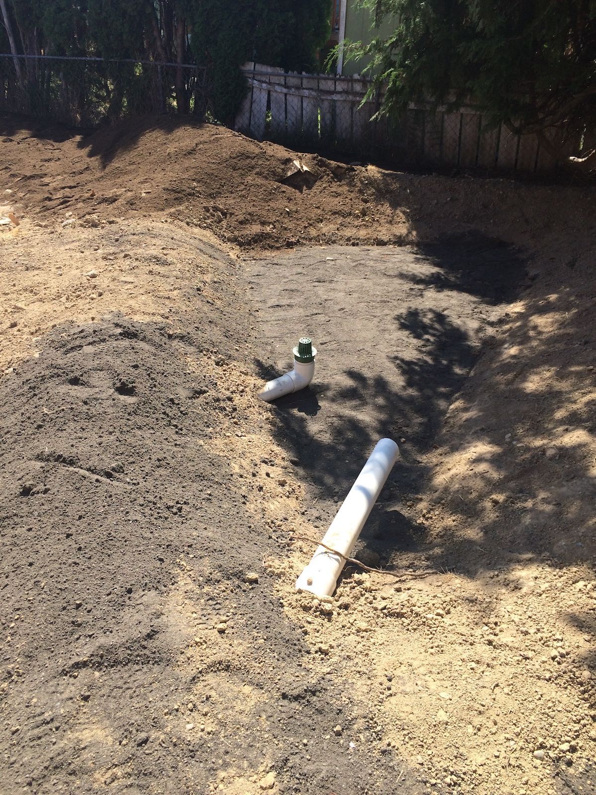 Exposed pipes and a green valve amidst a dirt yard during the construction phase of building a rain garden.