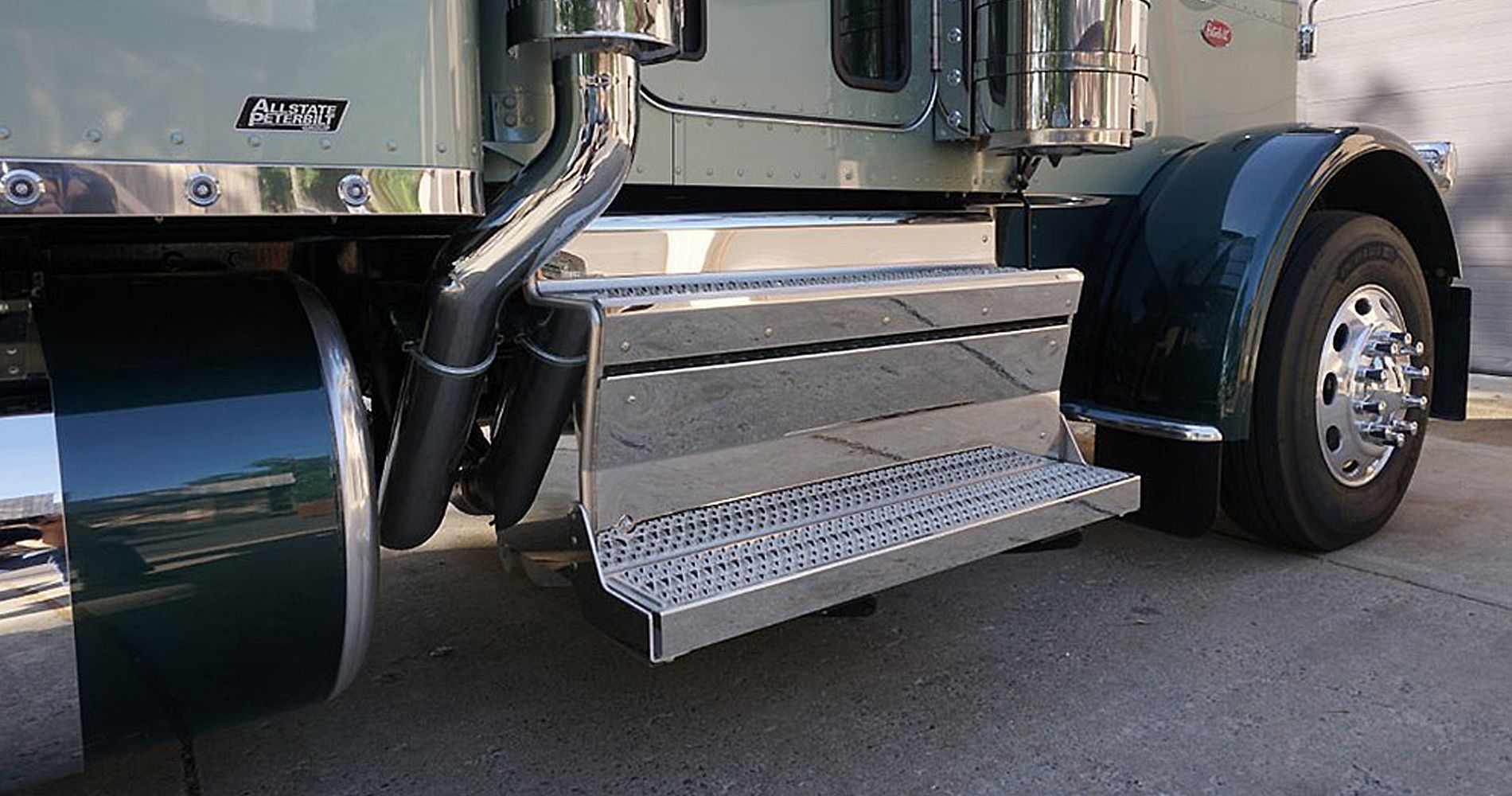 Side view of a green semi-truck with chrome steps and exhaust pipes.