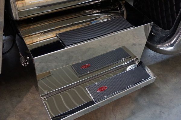 Shiny metal truck steps with black non-slip treads and a logo.