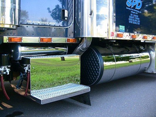 Shiny chrome fuel tank and step on a semi-truck; green grass in the reflection.