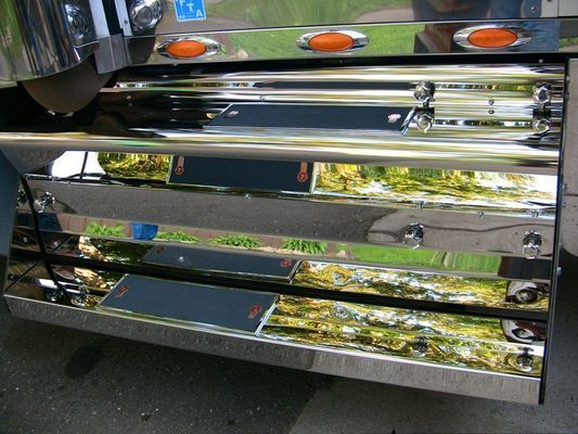 Chrome steps of a semi-truck with orange lights, reflecting greenery.