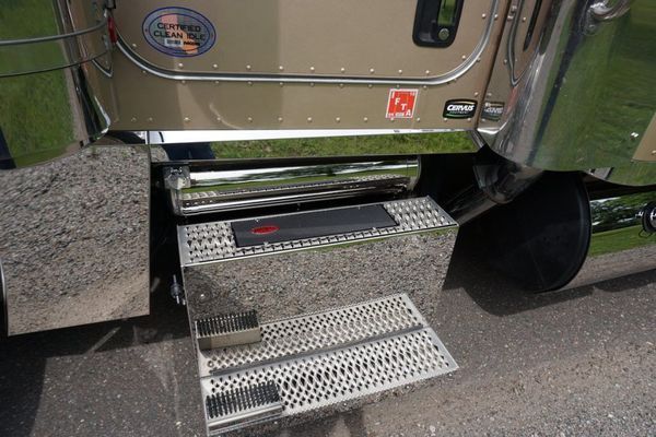Metallic truck step with treaded surface and chrome accents, below a cab.