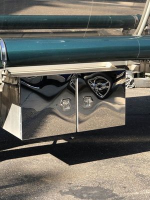 Shiny, chrome double-door toolbox mounted on a green trailer, casting a shadow on pavement.