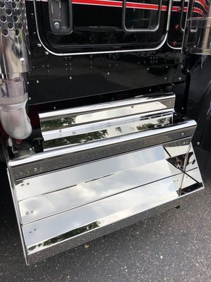 Chrome step on the side of a black semi-truck, reflecting the sky and surroundings.