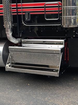 Chrome step of a black semi-truck, with red and black stripes, and chrome exhaust.