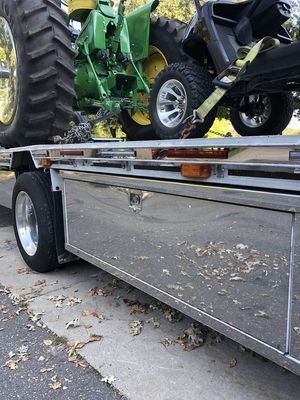 John Deere tractor and lawnmower on a flatbed trailer with a polished metal storage box.